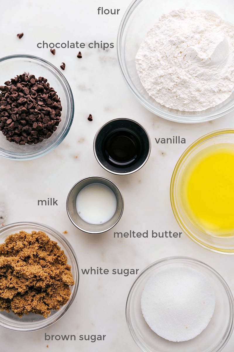 Array of ingredients arranged neatly, including flour, butter, brown and white sugar, vanilla extract, milk, and mini chocolate chips.