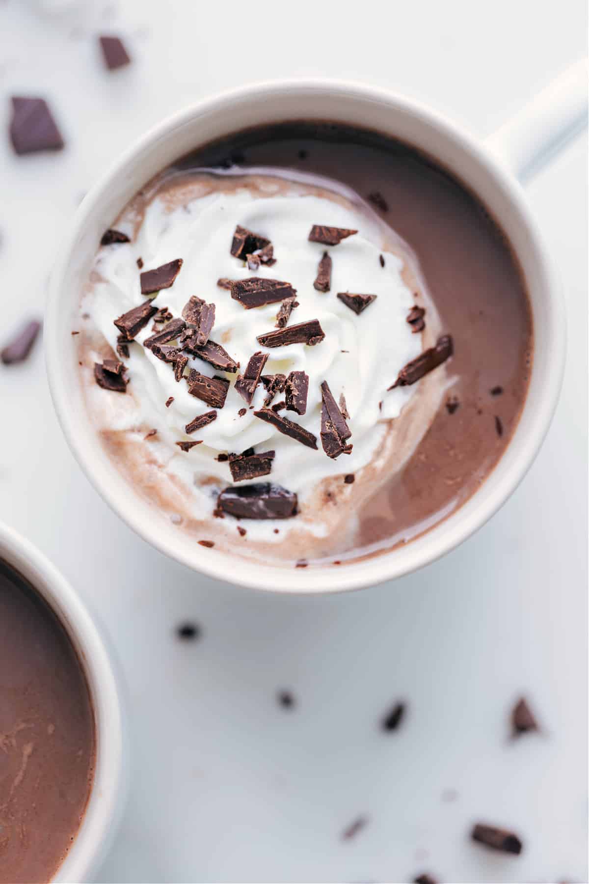 Mug of rich hot chocolate topped with a swirl of whipping cream and delicate chocolate shavings.
