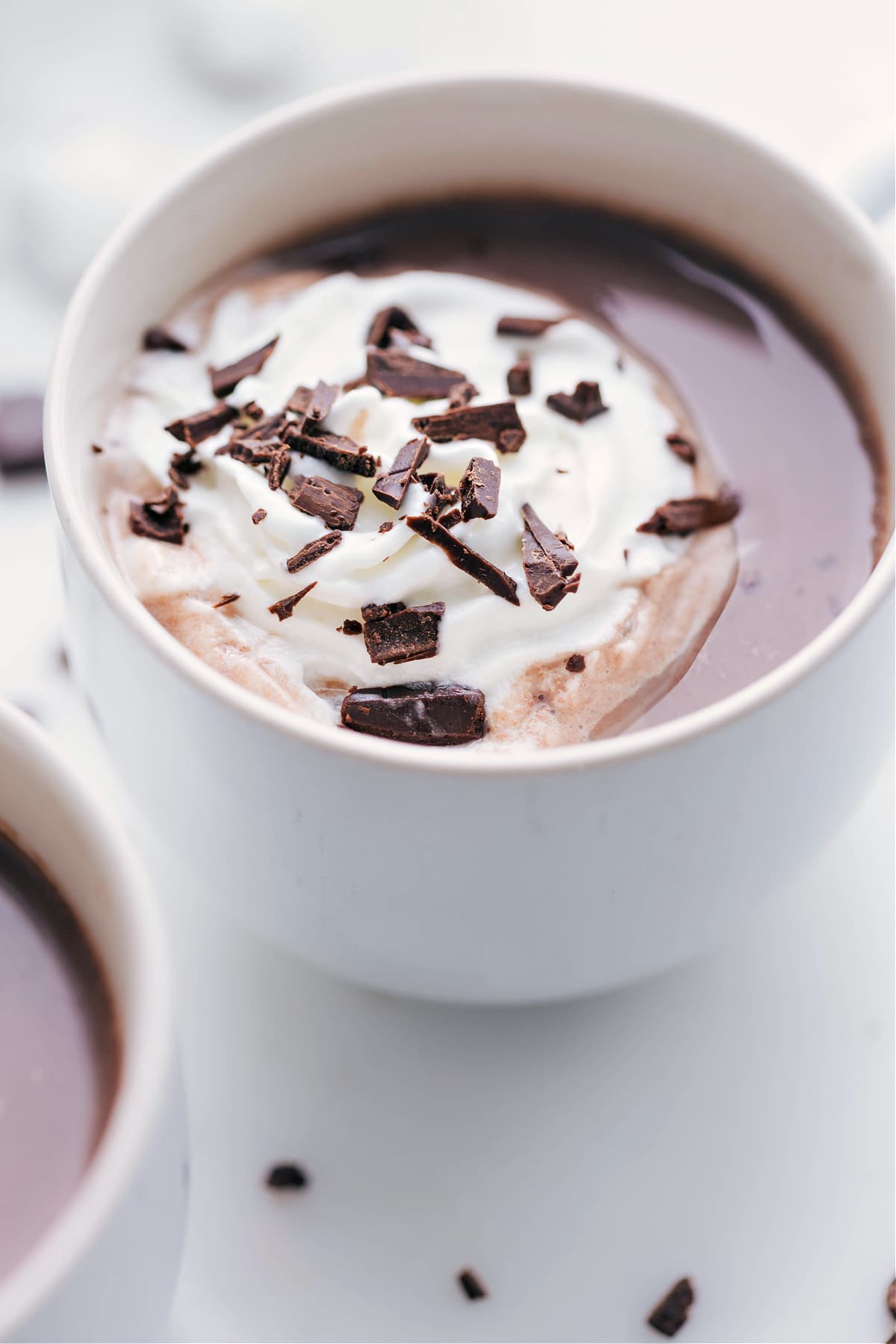 Mug filled with a delicious hot chocolate topped with a dollop of whipped cream and delicate chocolate shavings.