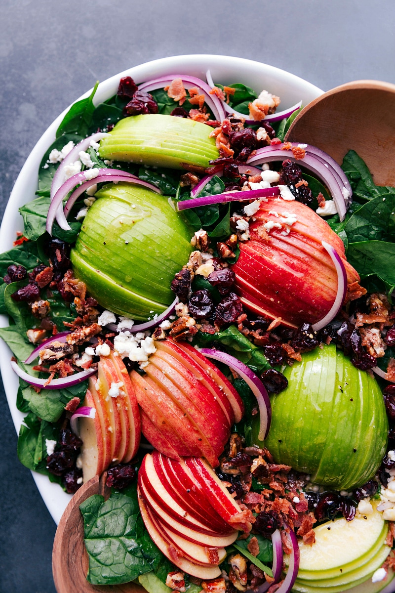 Overhead image of Spinach Salad, freshly dressed and ready to be eaten with serving spoons in the bowl.