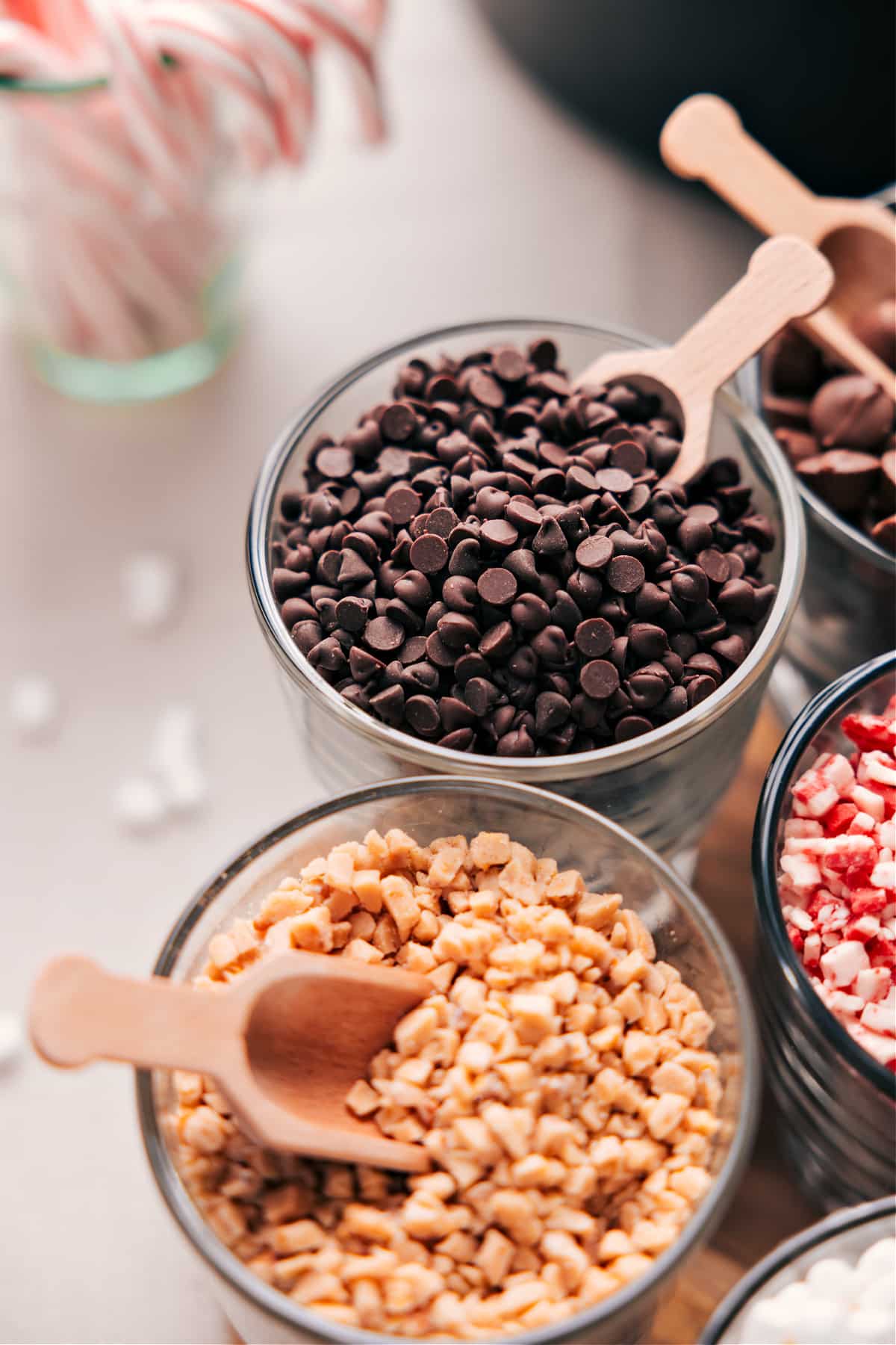 Two bowls side by side, one filled with chocolate chips and the other with crushed toffee pieces.