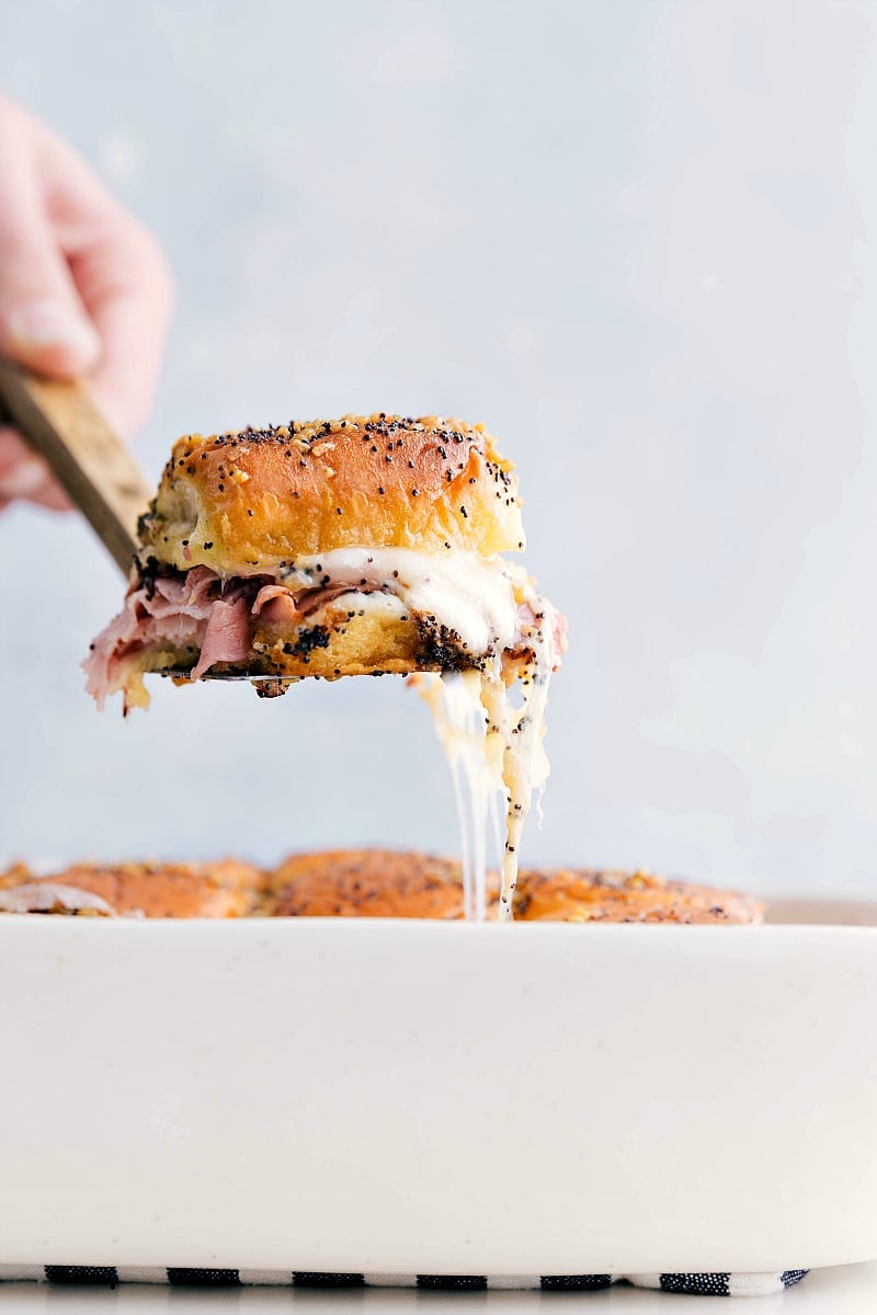 Ham and cheese sliders being picked up with a cheesy pull.