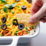 Ready-to-eat 7 layer bean dip being dipped into with a chip.