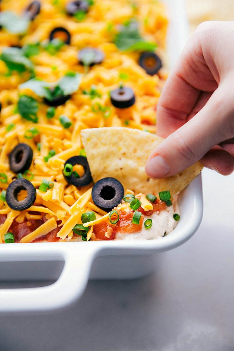Image of the ready-to-eat 7 layer bean dip being dipped into with a chip.