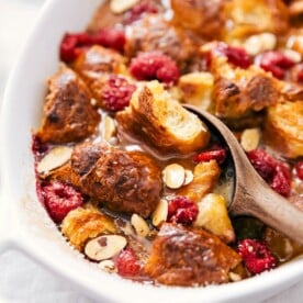 Scooping bread pudding with visible chunks of bread, drizzled syrup, and fruit pieces.