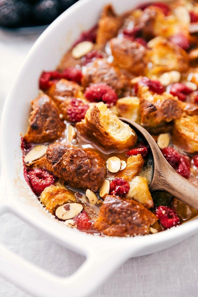 Scooping bread pudding with visible chunks of bread, drizzled syrup, and fruit pieces.