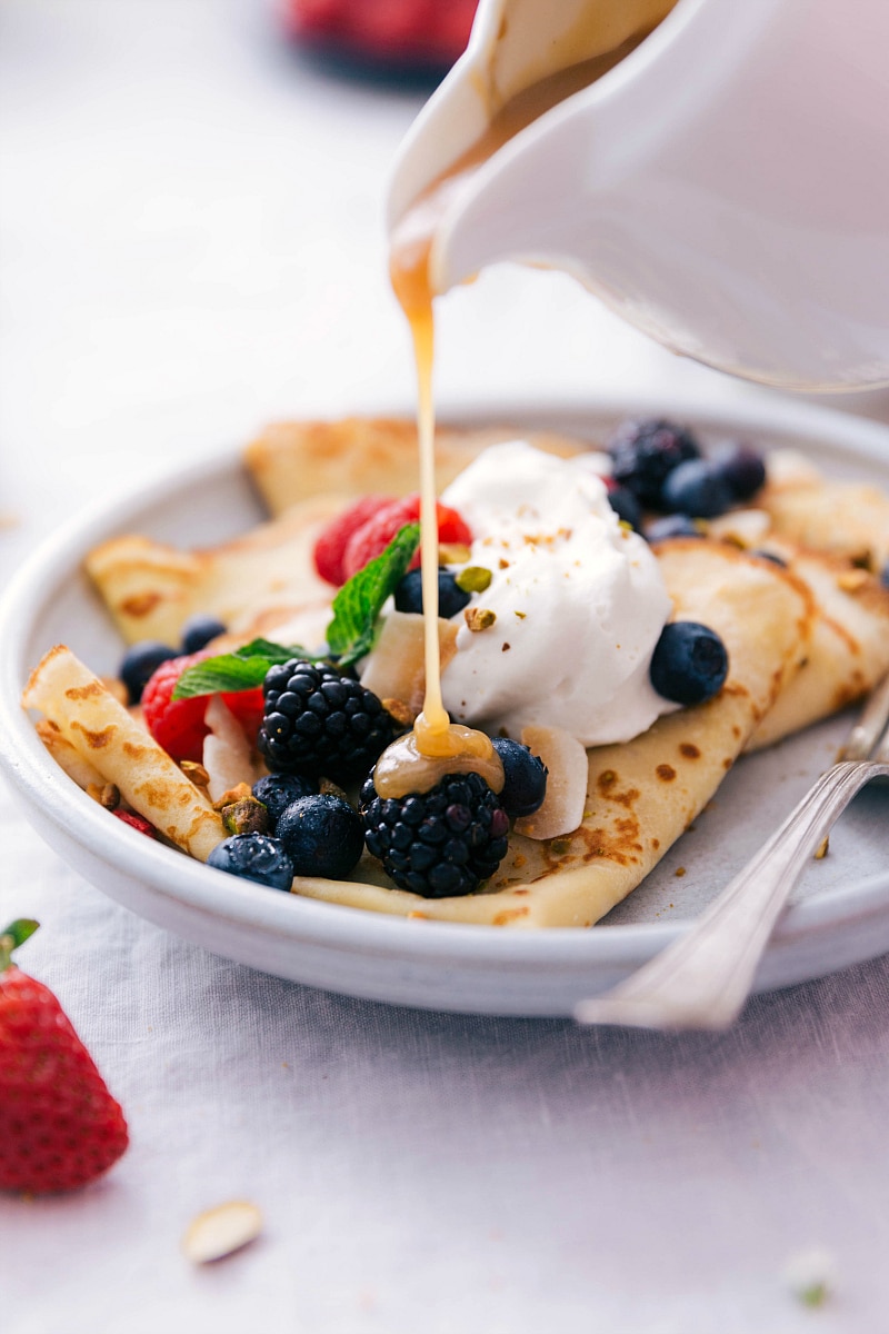 Image of vanilla syrup sauce being poured over the top of fruit-topped crepes.