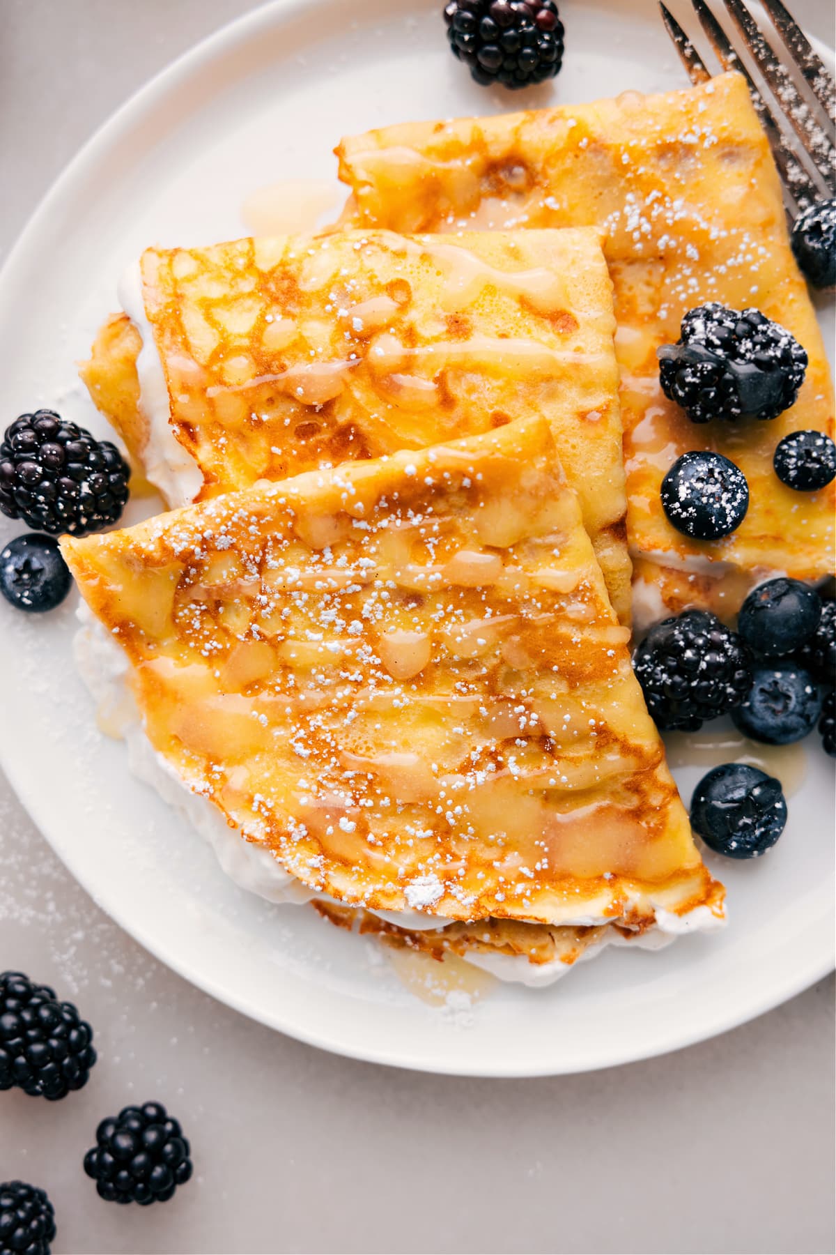 Plate of three crepes with berries and syrup drizzled on top.