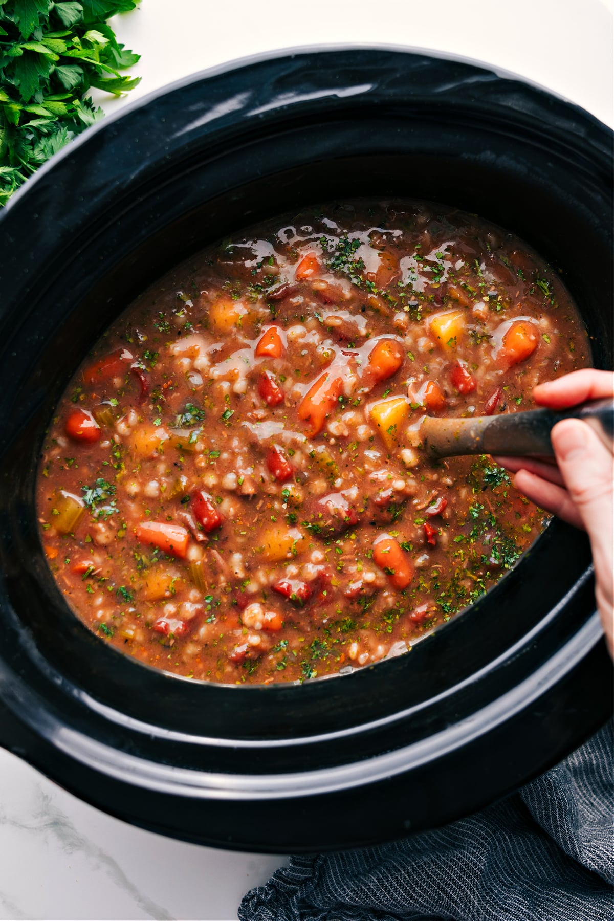 Simple And Delicious Slow Cooker Beef and Barley Soup Slow Cooker Beef and Barley Soup in the crockpot with a ladle full coming out.