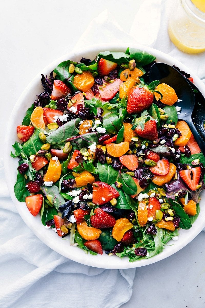 This refreshing orange and Strawberry Salad is packed with good-for-you ingredients and dressed in a flavor-packed citrus vinaigrette. This is one of my go-to salads to serve as a quick dinner side dish. There isn't too much prep required, it comes together exceptionally fast, and it's so versatile. Swap out the fruits, nuts, and cheese to your preference or what you have on hand. Plus, you can prepare the dressing ahead of time and use it all week long! Recipe via ChelseasMessyApron.com #vegetarian #salad #strawberry #mandarinoranges #strawberrysalad Overhead photo of a bowl of strawberry salad
