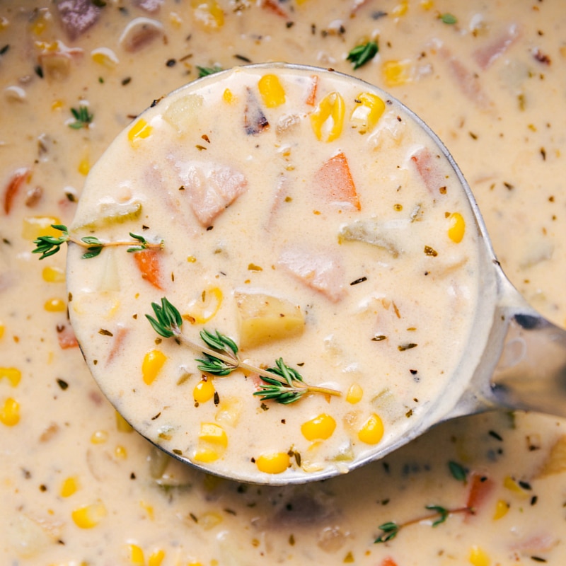 Close-up view of a big spoonful of Ham and Potato Soup, garnished with a sprig of thyme.