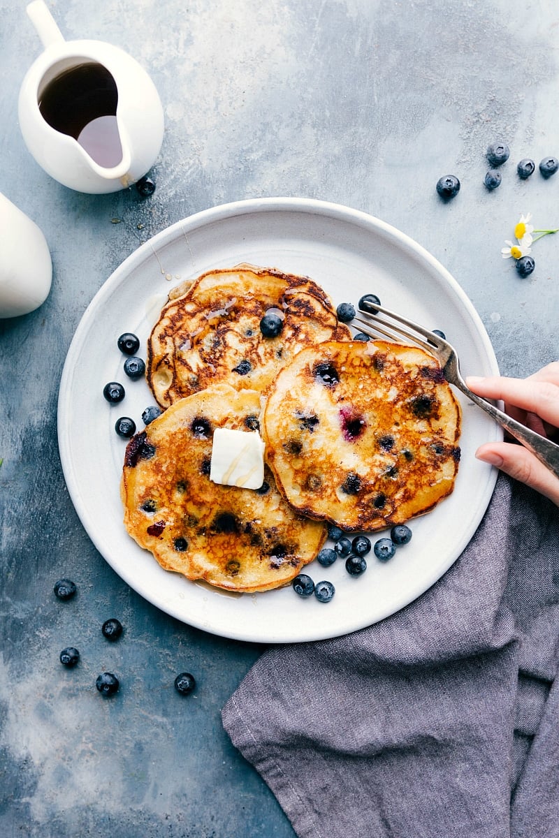 Ready to eat blueberry pancakes on a plate with butter and syrup on top and a fork on the side