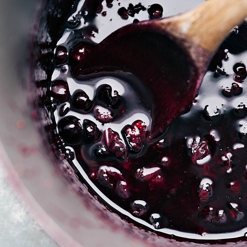 Up-close image of Blueberry Syrup on a wooden spoon, still in the saucepan.