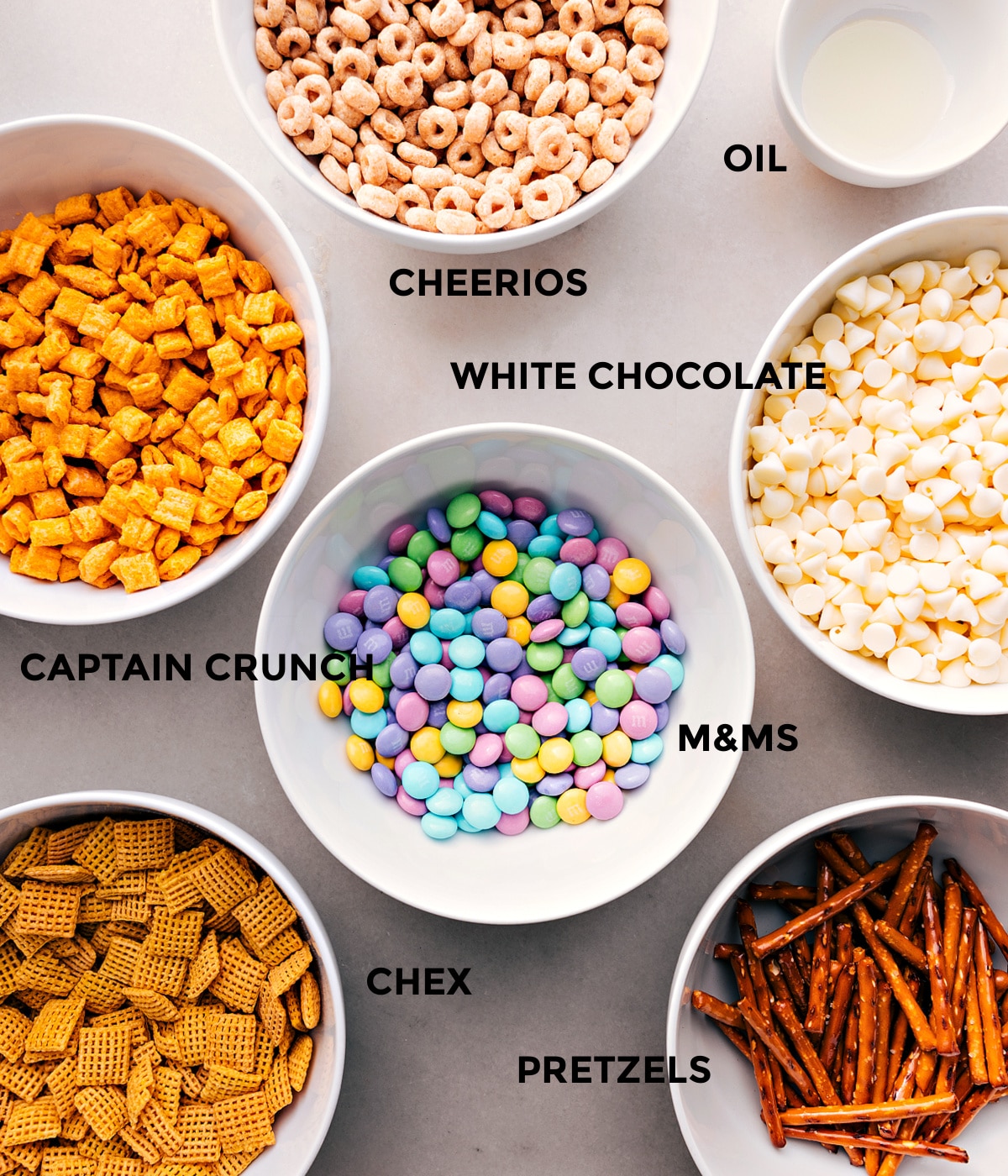 All the ingredients prepped and ready for easy assembly—Cheerios, oil, white chocolate, Cap’n Crunch, M&Ms, pretzels, and Chex cereal.
