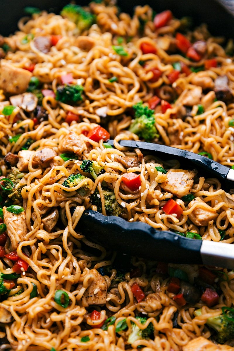 Fnished Chicken Ramen in a skillet with tongs holding some of the noodles.