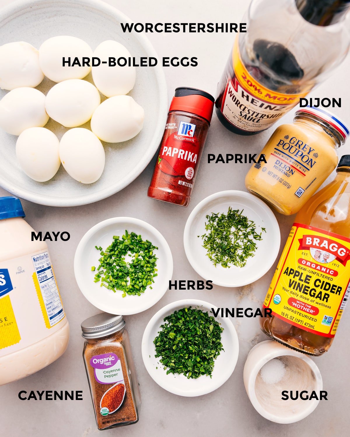 All the ingredients for this recipe are prepped and ready for easy assembly: eggs, Dijon, paprika, vinegar, herbs, mayo, seasonings, and sugar.