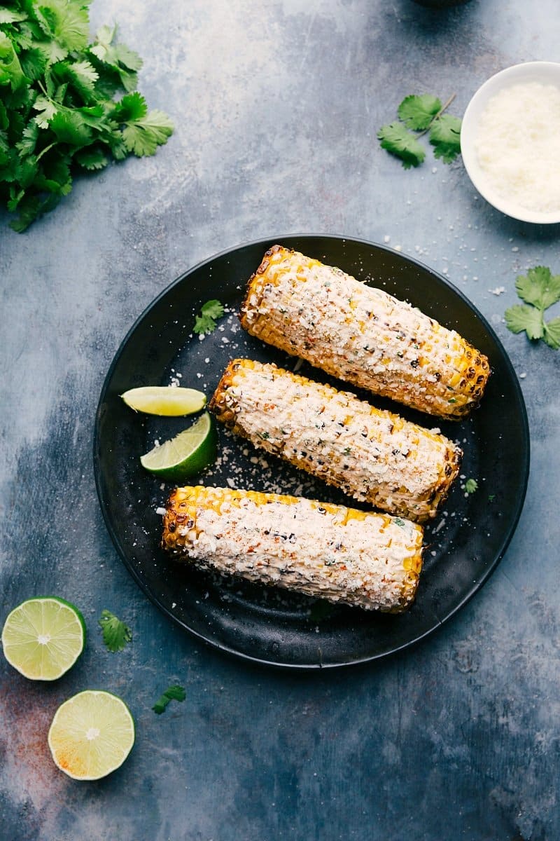 Image of the ready-to-eat Elote on a plate with limes and cilantro around them.