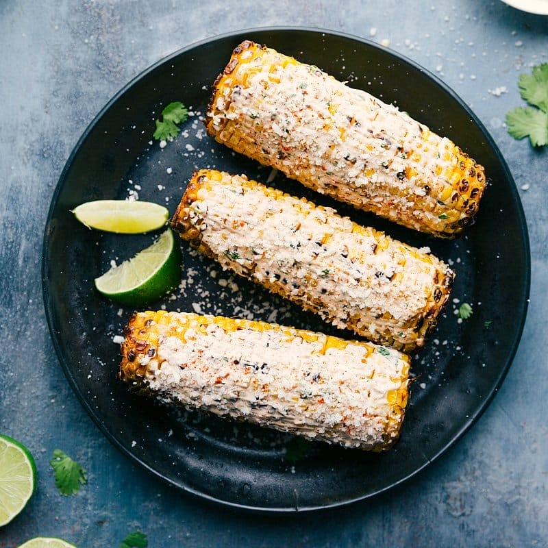 Image of Elote on a plate with lime wedges and cilantro on the side.