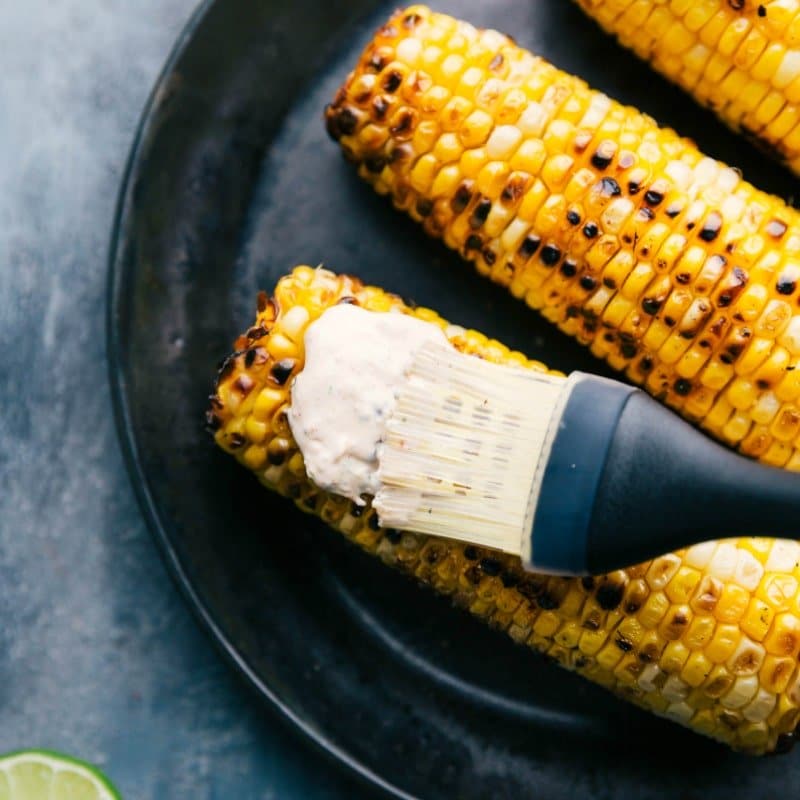 Image of the cream sauce being spread on the roasted corn for Elote.