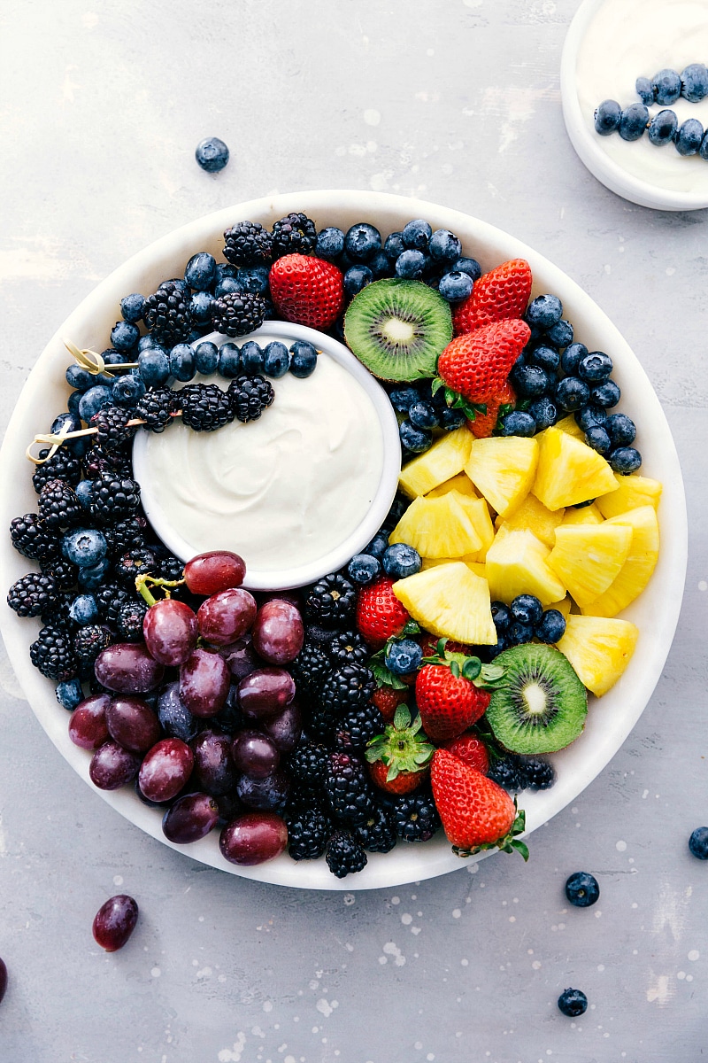 Only four ingredients go into this creamy, dreamy Fruit Dip! It's the perfect smooth, tangy, sweet accompaniment for fresh fruit! Recipe via chelseasmessyapron #withcreamcheese #withmarshmallowfluff #easy #recipe #fruitdip #dip #fruit #summer Image of the ready-to-eat Fruit Dip with a variety of fruit around it on a platter.