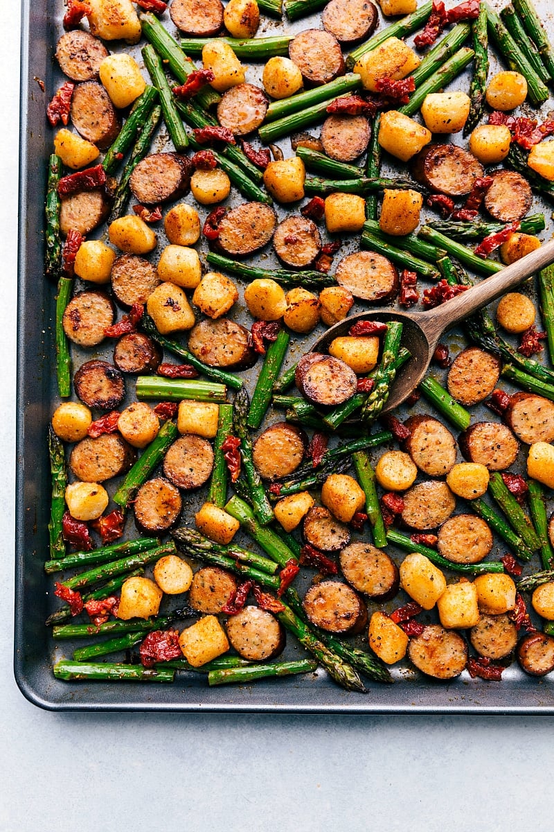 Picture of the finished pan of Sausage Pesto and Veggies with a spoon picking up some of the meal.