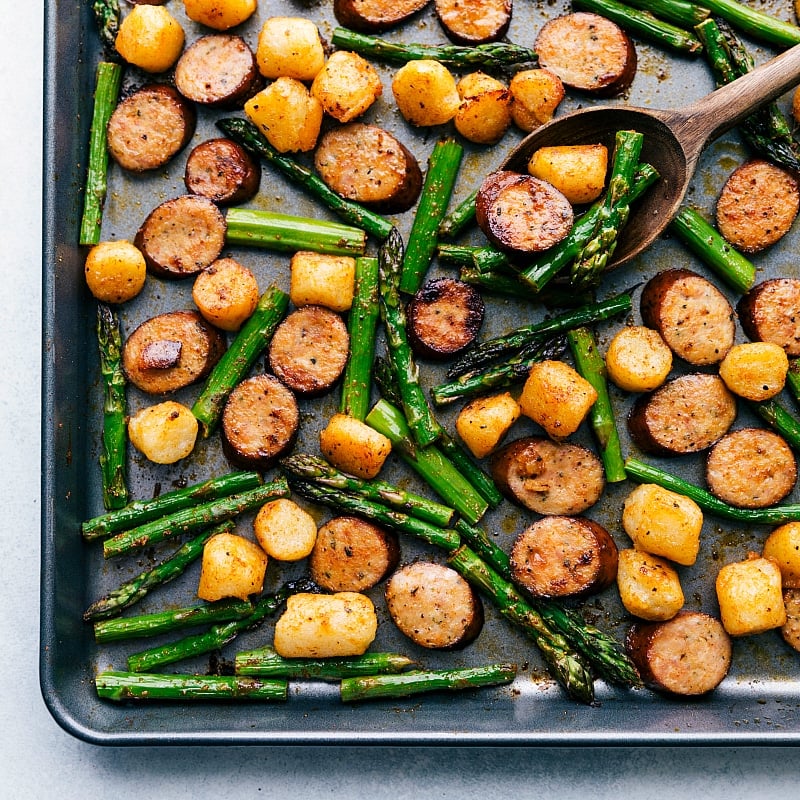 Process shot of meal: sausage, asparagus, and gnocchi roasting.