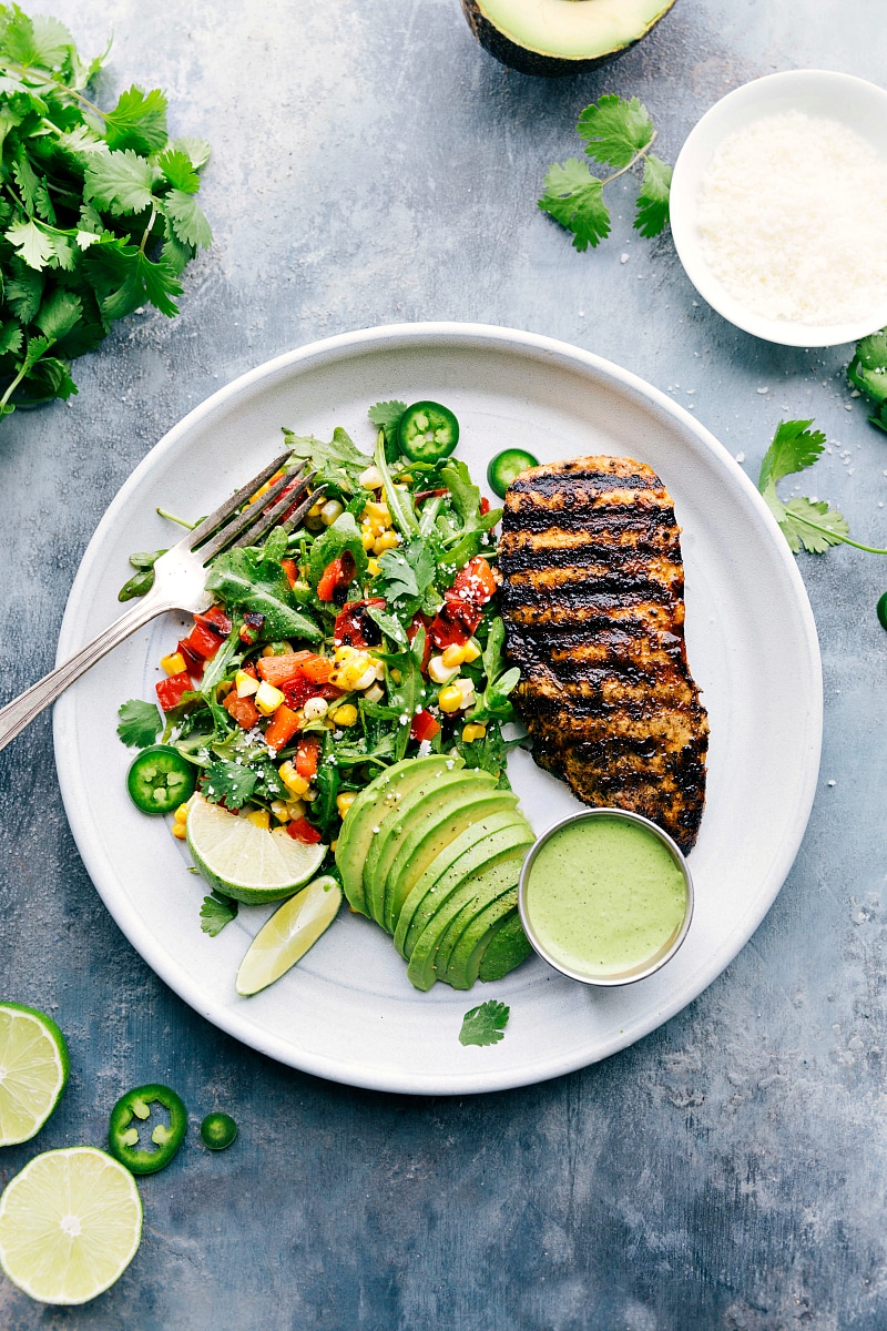 A plate filled with Peruvian chicken, a fresh salad, creamy avocado slices, and a vibrant green sauce, creating a healthy and delicious meal.