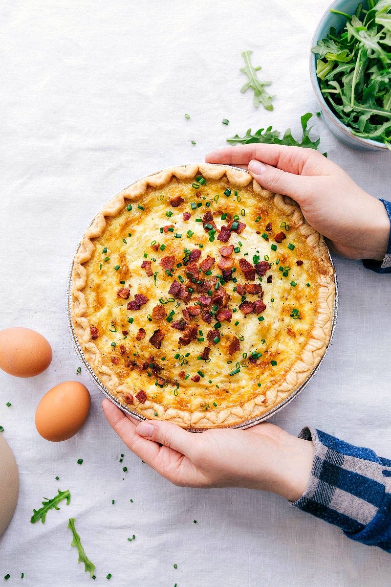 Finished Quiche Lorraine with herbs sprinkled on top, being held by two hands.