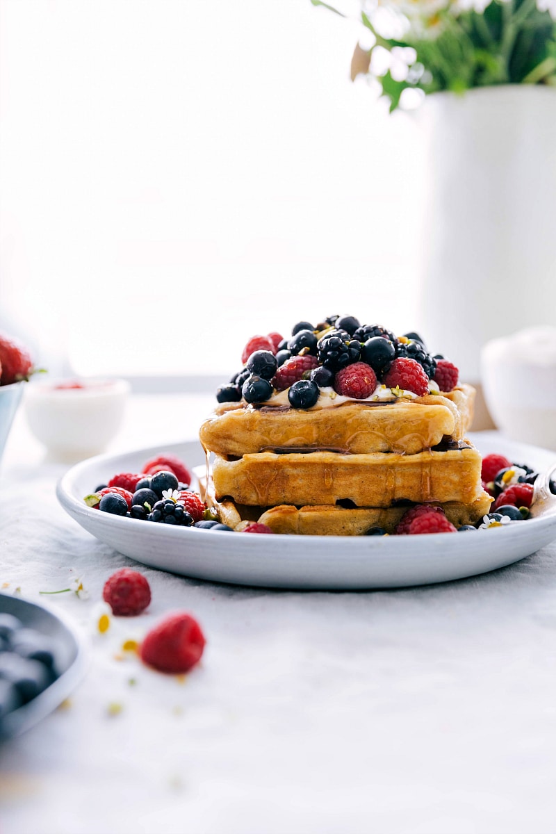 Stack of waffles with berries and whipped cream on top with syrup drizzling down.