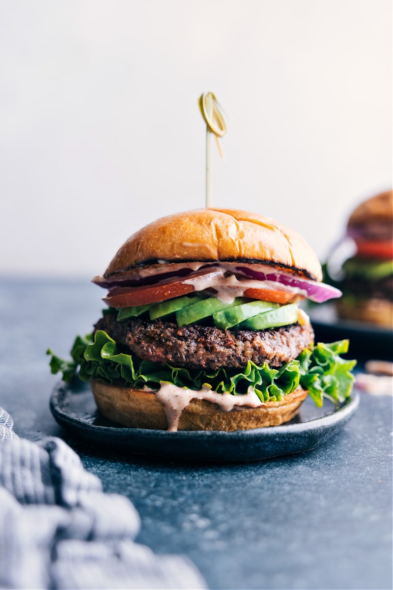Black Bean Burger with Fresh Vegetables and Sauce Plate with a delicious black bean burger, topped with a colorful array of fresh vegetables and flavorful sauce dripping down.