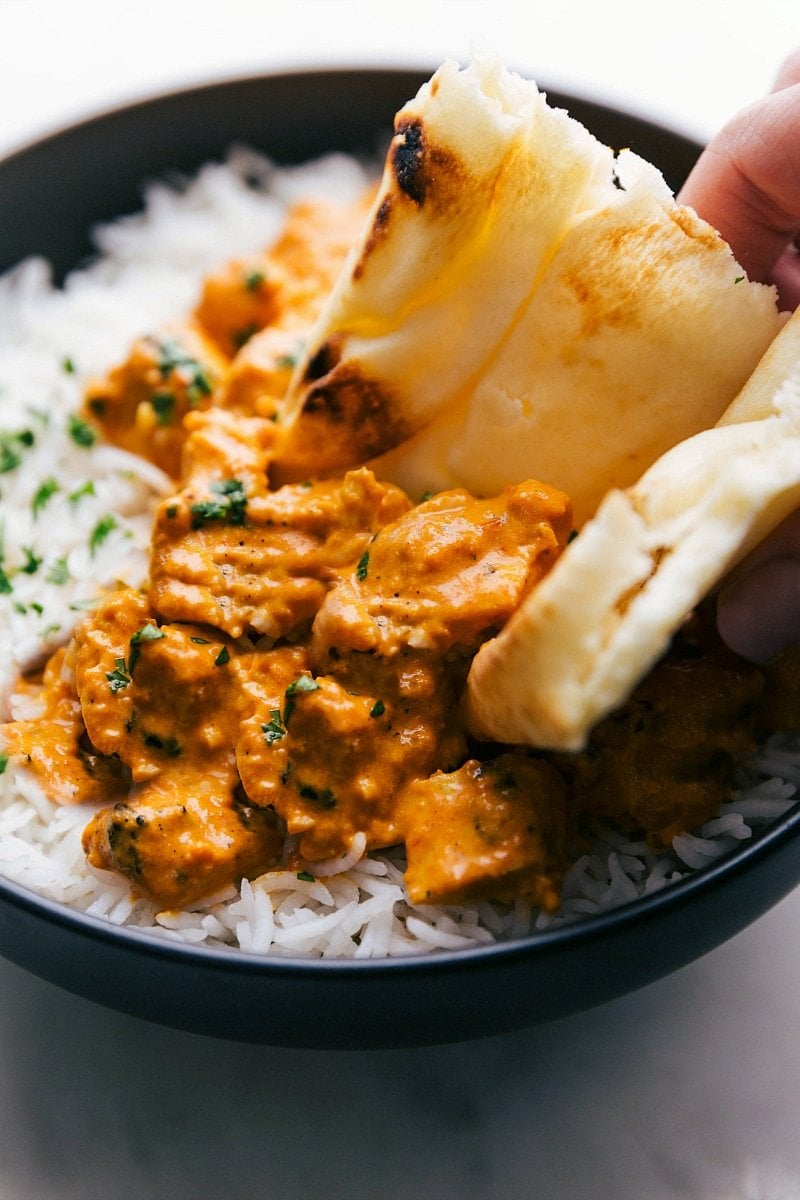 Naan bread scooping up chicken tikka masala served over basmati rice, showcasing a delicious and hearty meal.