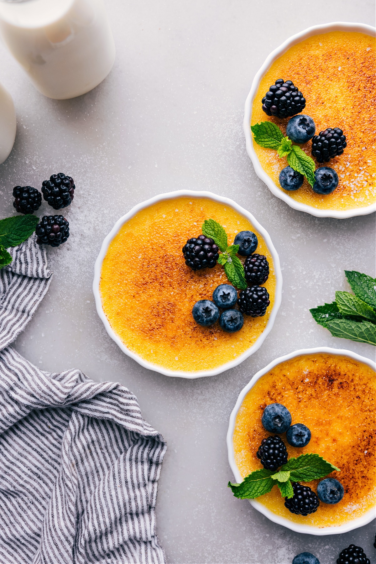 Golden creme brûlées with a crisp sugary top, garnished with fresh fruit.