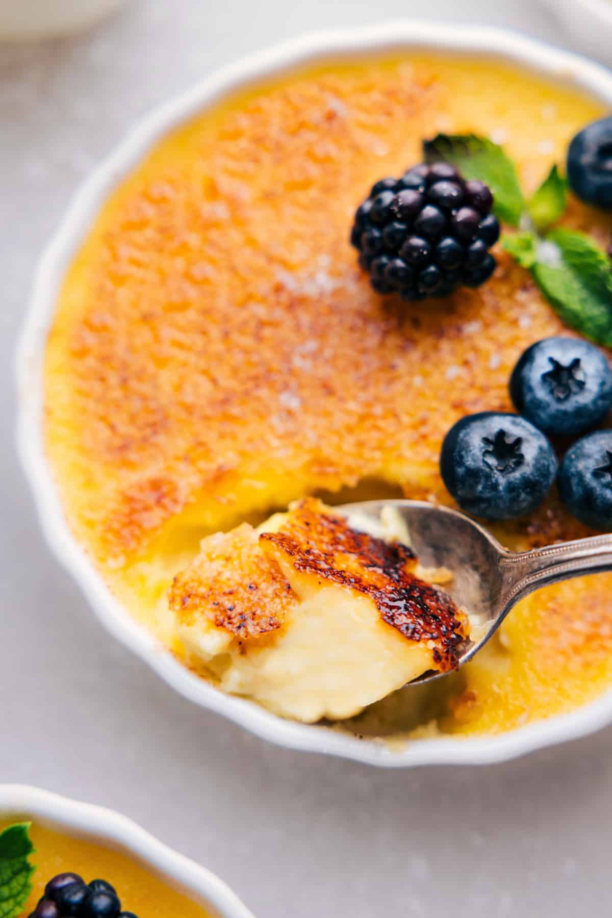 Finished creme brûlée with a perfectly caramelized top, spoon revealing its creamy center.