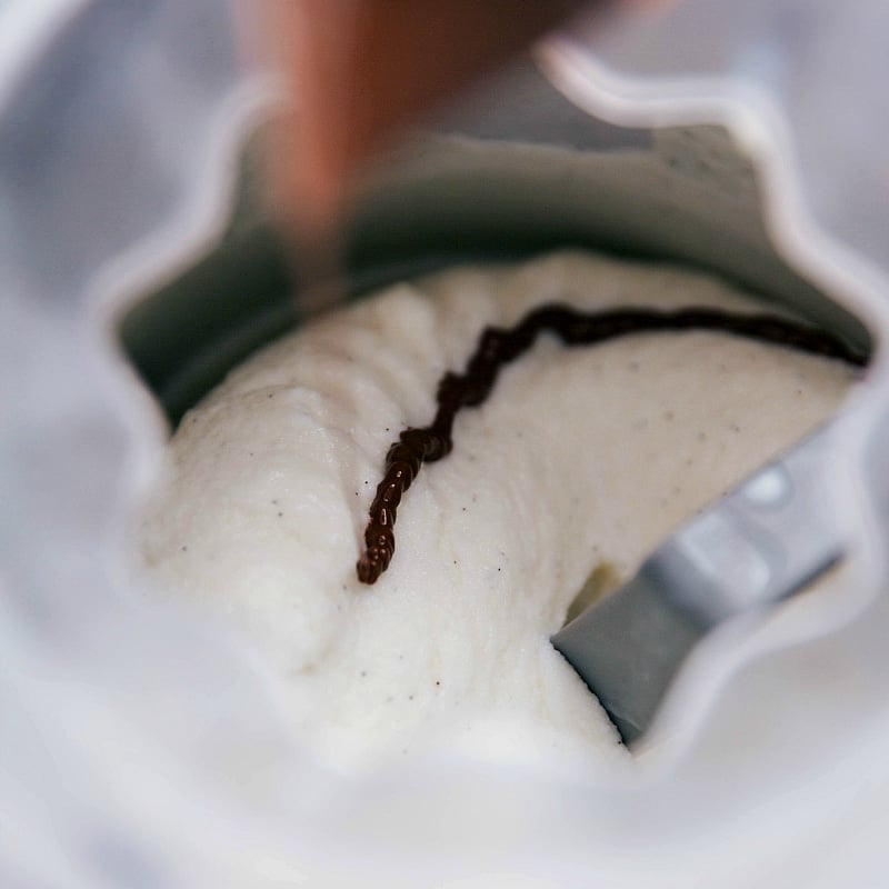 Chocolate being piped into the ice cream maker while churning to make stracciatella.