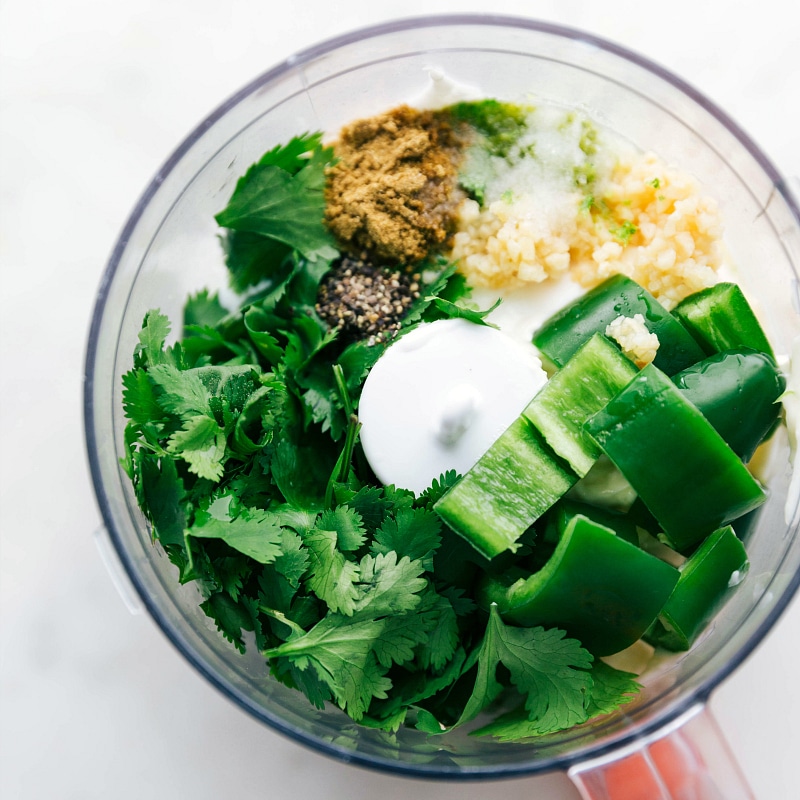 Overhead view of the inside of a food processor, showing the sauce ingredients for the grilled avocado bowls