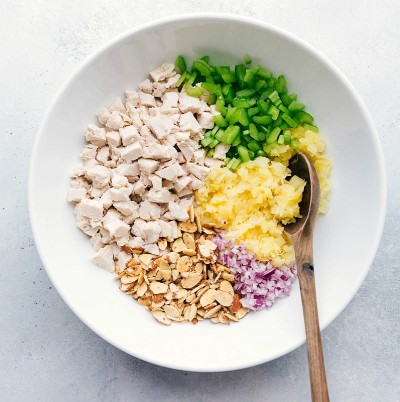 Process shot of bowl filled with chicken, pineapple, and other ingredients.