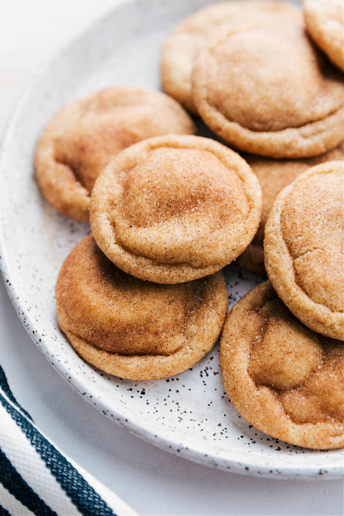 Snickerdoodle cookies arranged on a plate, fresh out of the oven, warm and inviting with a golden-brown exterior, dusted with cinnamon sugar, and packed with the best flavor.