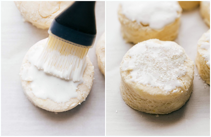 Heavy cream and coarse sugar being brushed and sprinkled on the tops of the biscuits before baking, enhancing their golden color and texture.