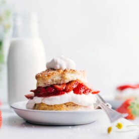Ready-to-eat Strawberry Shortcake with whipped cream on top and a fork on the side of the plate.
