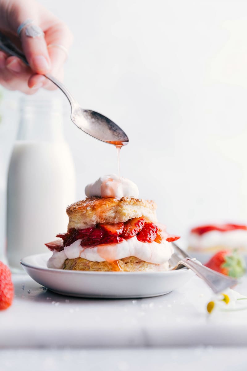 Moist and delicious strawberry shortcake with layers of fluffy cake, fresh strawberries, and whipped cream, strawberry sauce being drizzled on top.