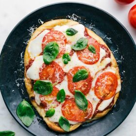 Naan Pizza on a plate, baked with basil on top.