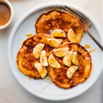 Banana Pancakes on a plate with fresh bananas and syrup drizzled on top.