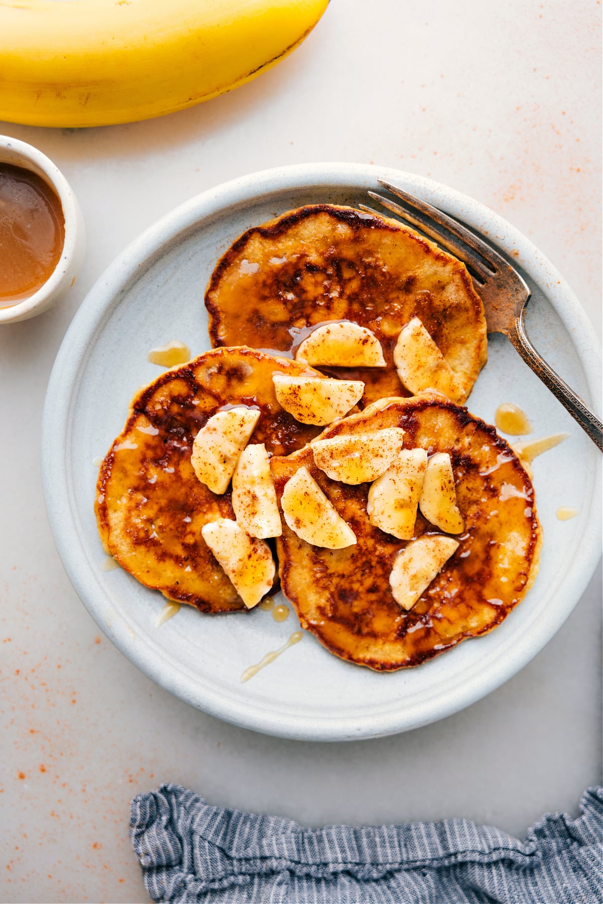 Banana Pancakes on a plate with fresh bananas and syrup drizzled on top.