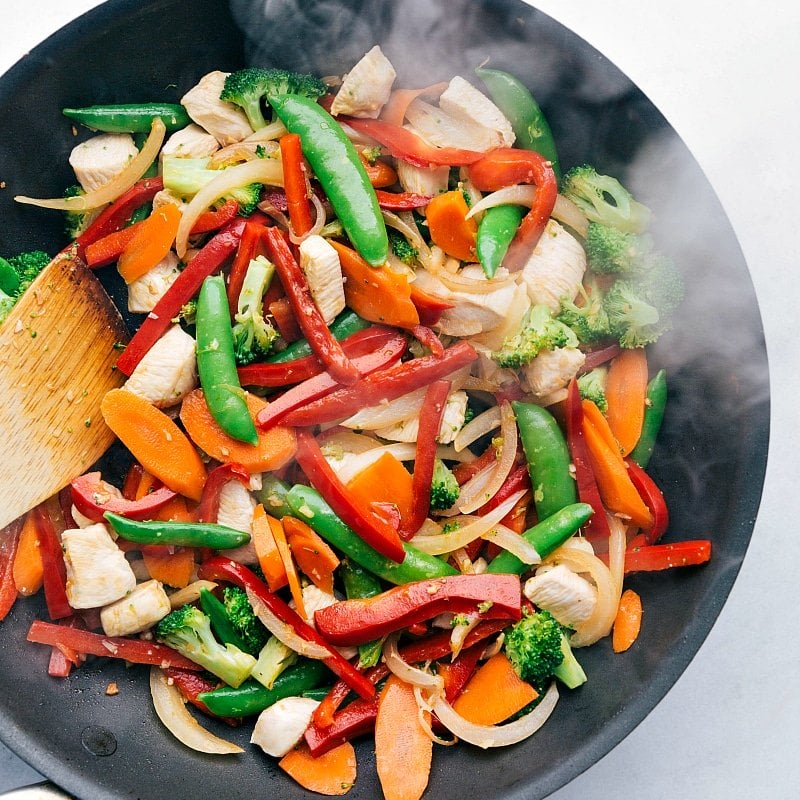 Mixing fresh vegetables and meat in the skillet.