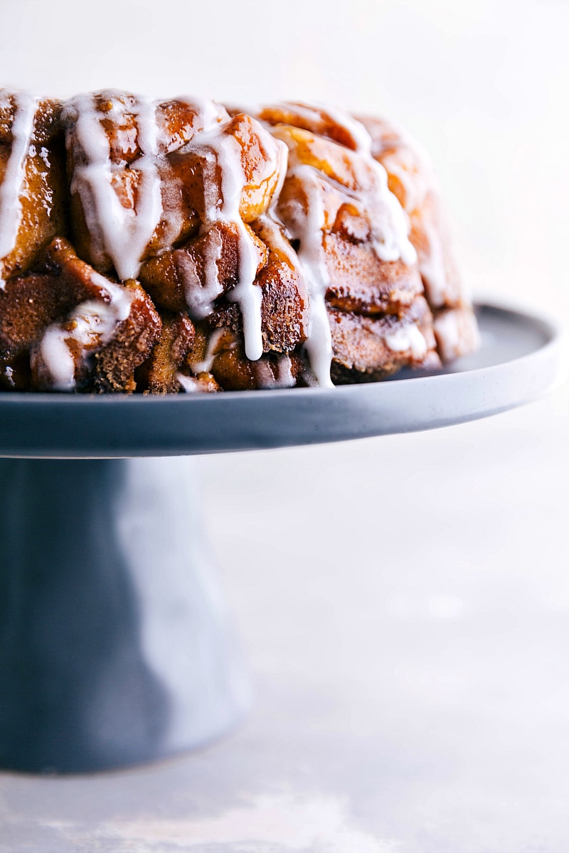 Image of Cinnamon Roll Monkey Bread with the frosting over it, on a cake stand, ready to eat .