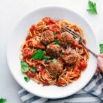 Bowl of finished Turkey Meatballs over spaghetti with sauce. Hand holding a fork ready to dig in.