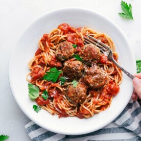 Bowl of finished Turkey Meatballs over spaghetti with sauce. Hand holding a fork ready to dig in.