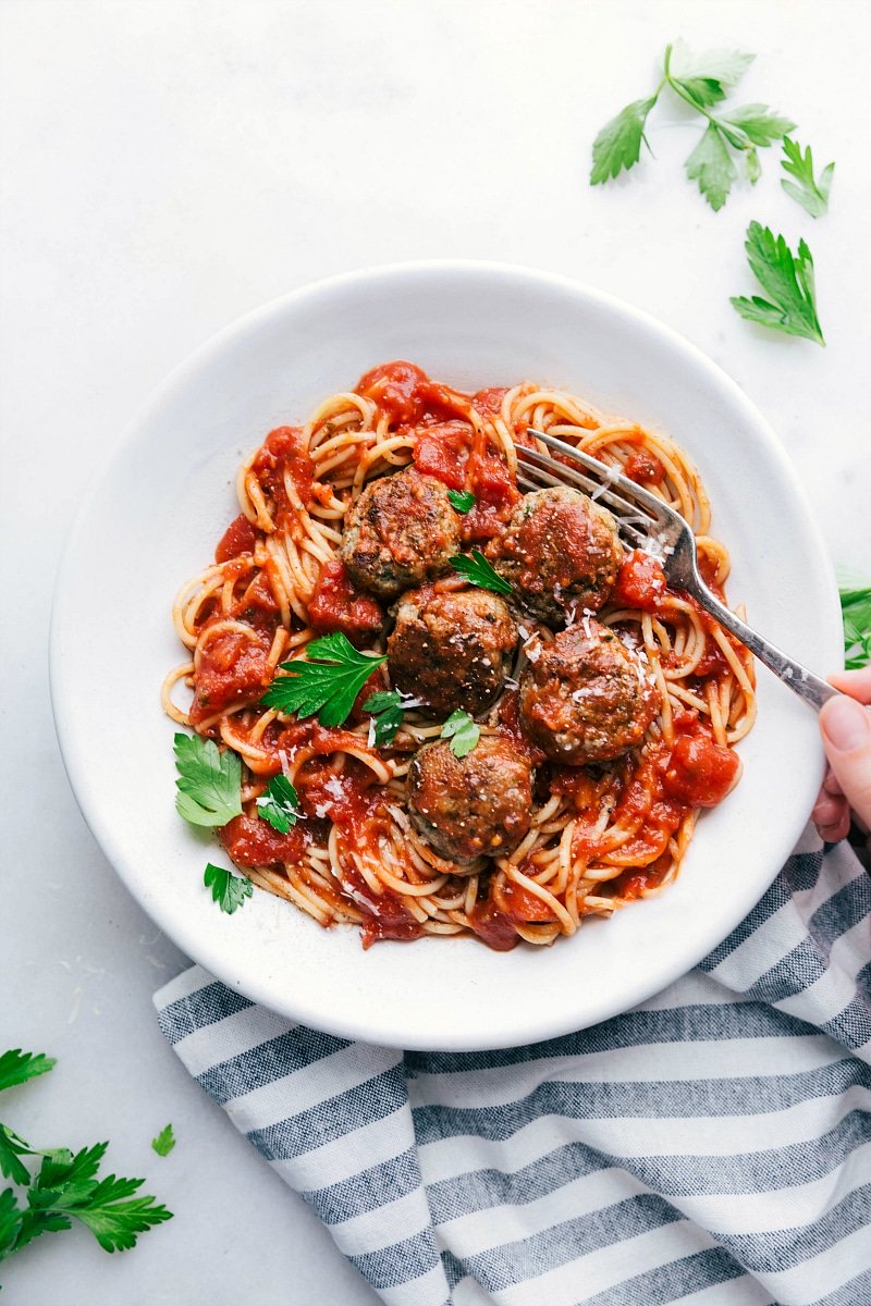 Bowl of finished Turkey Meatballs over spaghetti with sauce. Hand holding a fork ready to dig in.