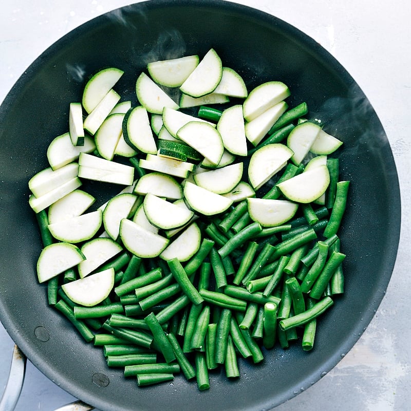 Uncooked zucchini and green beans in a skillet, ready for sautéing.