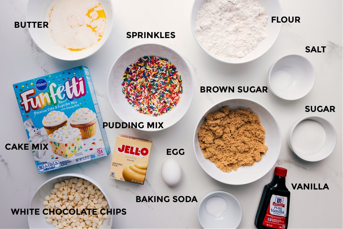 All the ingredients for this recipe prepped and ready for easy assembly, including butter, cake mix, sprinkles, pudding mix, flour, salt, sugar, brown sugar, vanilla, baking soda, and white chocolate chips.